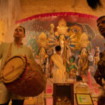 KOLKATA , INDIA - SEPTEMBER 27, 2017 : Young Hindu Priest worshipping Goddess Durga under holy smoke with dhaakis (drummers) performing. Durga Puja - shot at night under colored light .